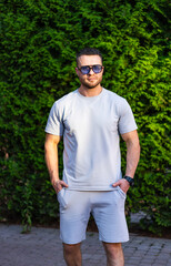 Man in casual summer outfit. Male in a light gray outfit stands confidently against a lush green...