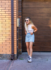Young woman enjoying sunny day at home. A woman stands by a brick wall outside her house, smiling...