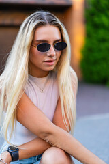 Summer fun for young woman. A young woman with long blonde hair sits casually, wearing sunglasses...