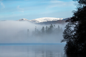 Fairfield in snow beneath a bright sky above a cloud inversion from the shores of Windermere