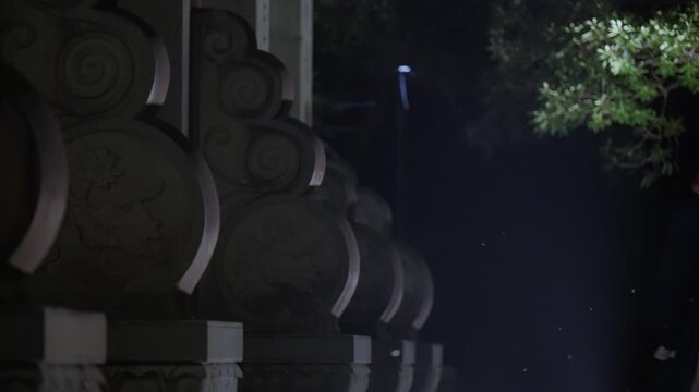 Nighttime stone colonnade with illuminated arches and overlapping tree shadows creating atmospheric depth