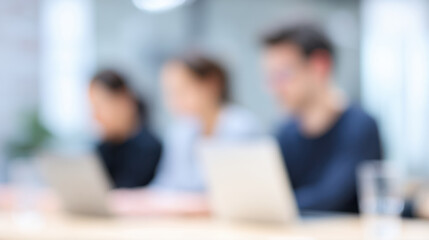 Blurred depth of field shot of office team working on laptops in modern workspace with natural light creating focused and productive atmosphere