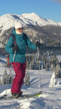 CLOSE UP: Young female tourist on splitboarding trip hikes up a snowy hill. Fit Caucasian woman ski touring in Velika Planina on a perfect sunny winter day. Splitboarder ascends up a scenic mountain.