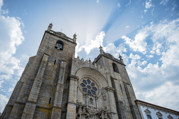 Fototapeta premium Perspective view of the facade and rose window of Porto Cathedral backlit with rays of sunlight filtering through the clouds
