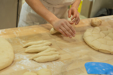 Baker shaping dough on wooden surface with flour and tools in a cozy kitchen environment
