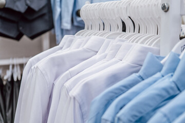 neatly arranged dress shirts hang from hangers in clothing retail store, featuring various light colors for children. school uniform simple and comfortable. sale. close up.