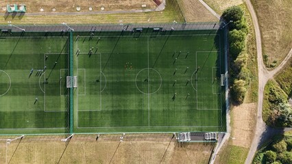 Birds eye aerial drone view of football pitch with players playing soccer match on green sports...