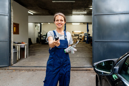 Female auto mechanic giving car key to client at auto repair shop