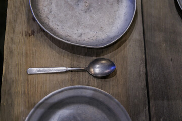 Aluminum bowl with a spoon on the background of wood. An old aluminum plate on wooden boards.