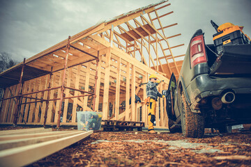 Construction of a Wooden House With a Worker and a Pickup Truck Nearby