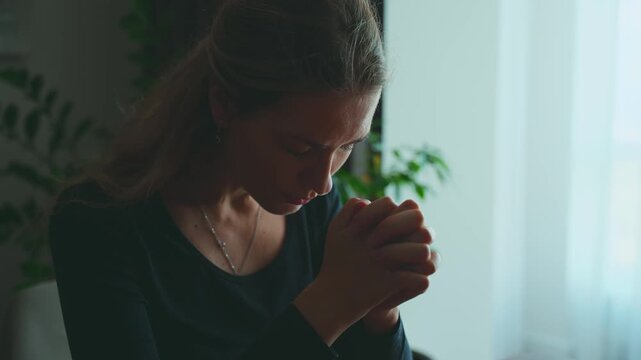 Portrait adult woman praying before reading Holy Bible, hands folded in prayer. Dark silhouette female prayer. home room window. Girl Christian praying to God, concept of religion faith hope blessing