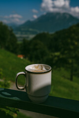 A warm cup of creamy cappuccino enjoyed in the quiet morning mountains &mdash; soft foam, rich aroma, and breathtaking views in Alps Mountains create the perfect start to inspiring day