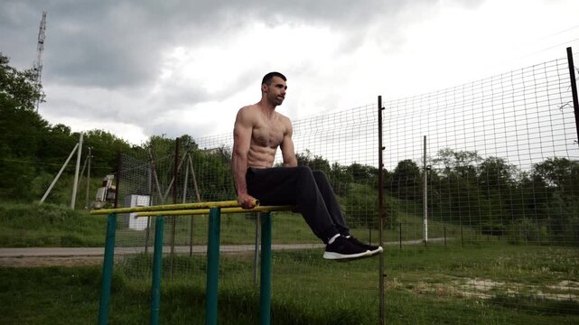 Strong guy training abdominal muscles on parallel bars at sports ground. Young shirtless sportsman exercising at nature. Sporty athlete working out at nature. Concept of active sportive lifestyle