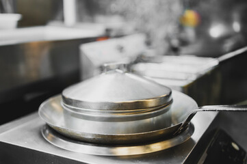 Stainless steel pan with lid and spatula on stovetop in commercial kitchen. Clean, professional...