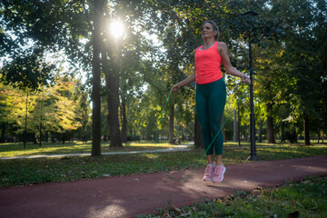 Fototapeta premium Fit woman jumping rope outdoors in park, sunlight workout for healthy active lifestyle.