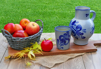 Äpfel und traditioneller hessischer Tonkrug mit Apfelwein auf einem Tisch im Garten.