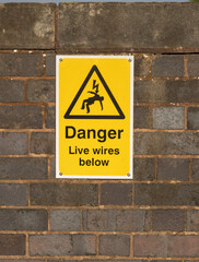 Brightly colored yellow sign mounted on a brick wall with a warning about live electrical wires...