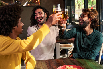 Three cheerful multiracial group of male friends at bar, toasting with beers, having fun together, laughing. Image with copy space.