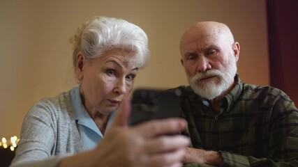 Senior couple shocked reading utility bill on phone, worried about high expenses - Powered by Adobe