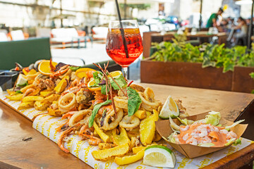 Italian alcoholic drink Aperol spritzer with a slice of lemon and a board with seafood