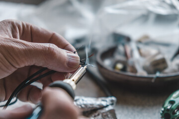 person meticulously solders wires together, showcasing craftsmanship. workspace features various...
