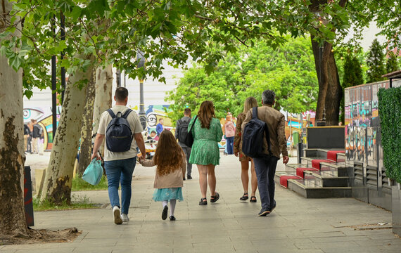 A group of people are walking down the street. A father leads his daughter by the hand as they walk down the street. Men and women walking in the city. People on the street.