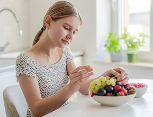 Teen Girl Eating Grapes At The Kitchen Table At Home