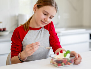 Smiling Girl Eating Fruit Salad At Home In The Kitchen