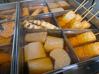 A pot of oden with assorted ingredients like daikon, fish cakes, and skewers simmering in...