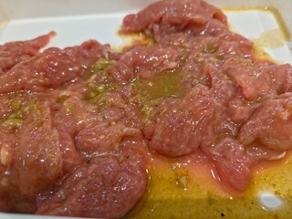  Raw beef that appears to be marinated or coated in a sauce,  preparation for cooking.