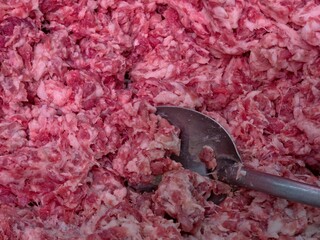 Close-up, top-down shot of a large pile of ground pork meat, with a metal scoop or large spoon...