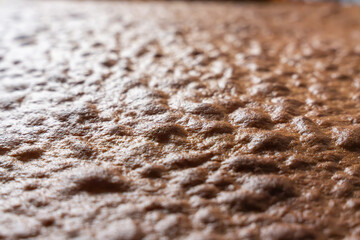 Oblique view of a cake surface with an uneven texture. The light highlights the golden brown crust.