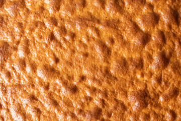 Detailed shot of a baked cake surface with a crispy, golden crust. The irregular texture reveals the airy batter.