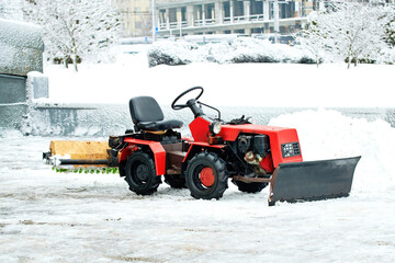 Red tractor with snow brush cleaning frozen driveway during cold winter season, utility vehicle, road maintenance,  outdoor street clearing. Snow removal process with red tractor and brush machine