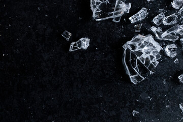 Fragments of shattered glass on dark surface with reflective light play