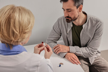Hearing care professional tells male patient how to use hearing aid and how to maintain them and change the battery. Hearing aid selection
