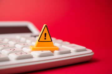 Yellow warning sign on white calculator with red background copy space. Personal, household or...