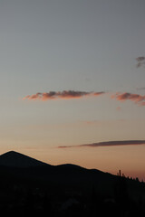 A vertical shot of a serene mountain silhouette against a pastel sky at sunset, with thin clouds illuminated by the warm light, creating a peaceful, minimalist scene.