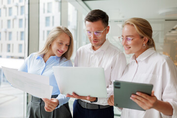 Business team collaborating on a laptop, discussing documents near a window.