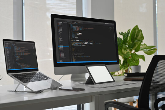Professional programmer workspace with desktop, laptop, and tablet showing HTML and CSS code in an office