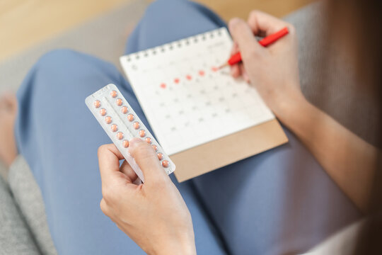 A young female holding birth control pills and a period schedule on the calendar plans to take a pill to control birth. - Powered by Adobe