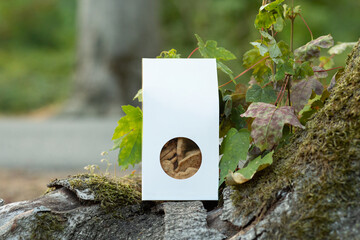 White paper food packaging box with transparent window standing on a tree trunk surrounded by green...