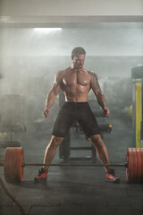 muscular man is preparing to lift a heavy barbell in a gym. He stands determined with his feet...