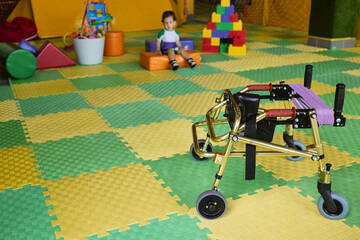 Gold walker mobility device is positioned in a therapy space designed for children's physical...