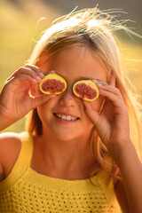 Blonde girl holding fig halves to her eyes on a sunny day, laughing and playing playfully,...