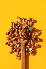 Different nuts, walnut, hazelnut, almond in wooden spoon on yellow background flat lay top view....