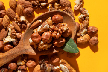 Different nuts, walnut, hazelnut, almond in wooden spoon on yellow background flat lay top view. Mix of tasty healthy nuts, snack, appetizer. Sunlight with long shadows
