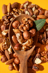 Different nuts, walnut, hazelnut, almond in wooden spoon on yellow background flat lay top view. Mix of tasty healthy nuts, snack, appetizer. Sunlight with long shadows