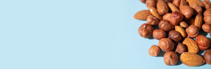 Scattered nuts hazelnuts and almonds on blue background flat lay top view. Food background. Tasty healthy snack, appetizer. Peeled nut kernels, dried fruit. Space for text. Long banner