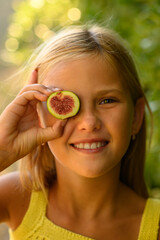 Blonde girl holding fig halves to her eyes on a sunny day, laughing and playing playfully,...